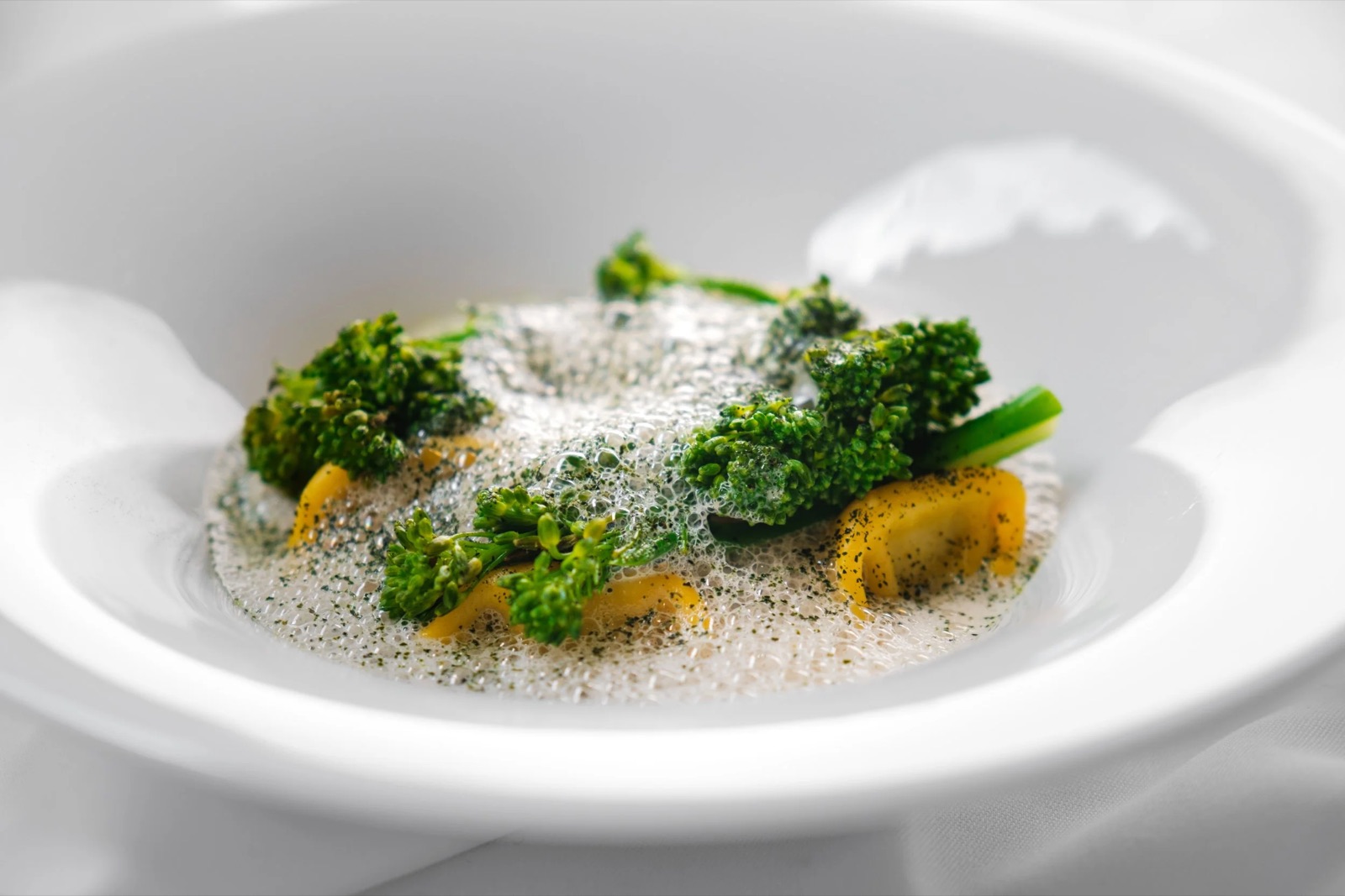 Djup vit tallrik med gula pastabitar, broccolini och ljus skummande buljong